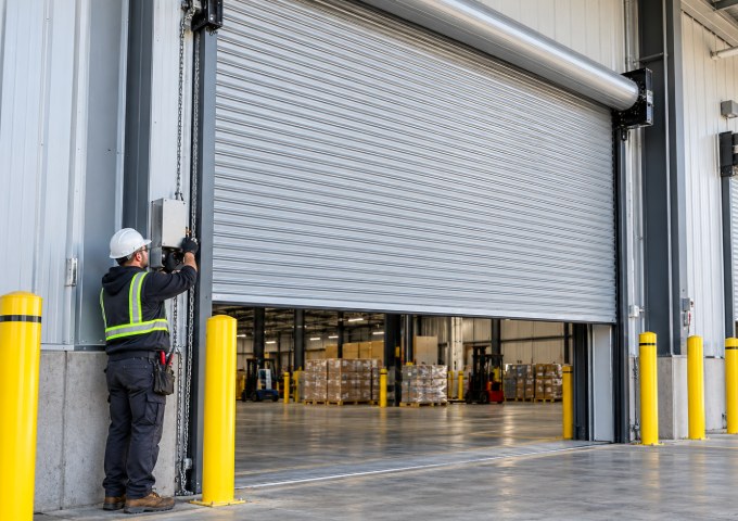 Technician in a hard hat checking the chain hoist and controls of a warehouse rolling door